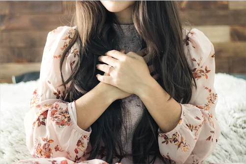 Lady with long black hair holding hands in front of heart